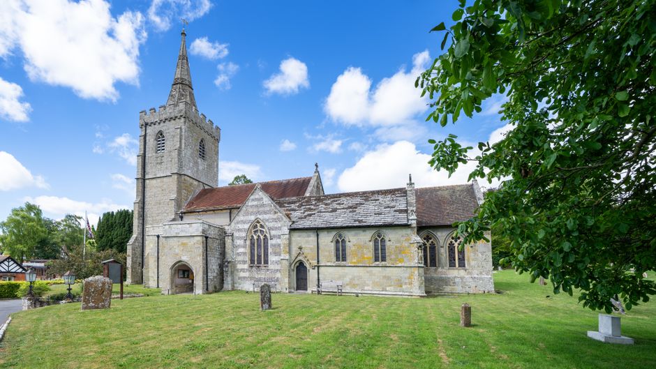 A detailed image of a floral arrangement featuring a bouquet of fresh flowers placed on a table in front of St Mary Church in West Wickham. The bouquet includes pink roses, white lilies, and purple st