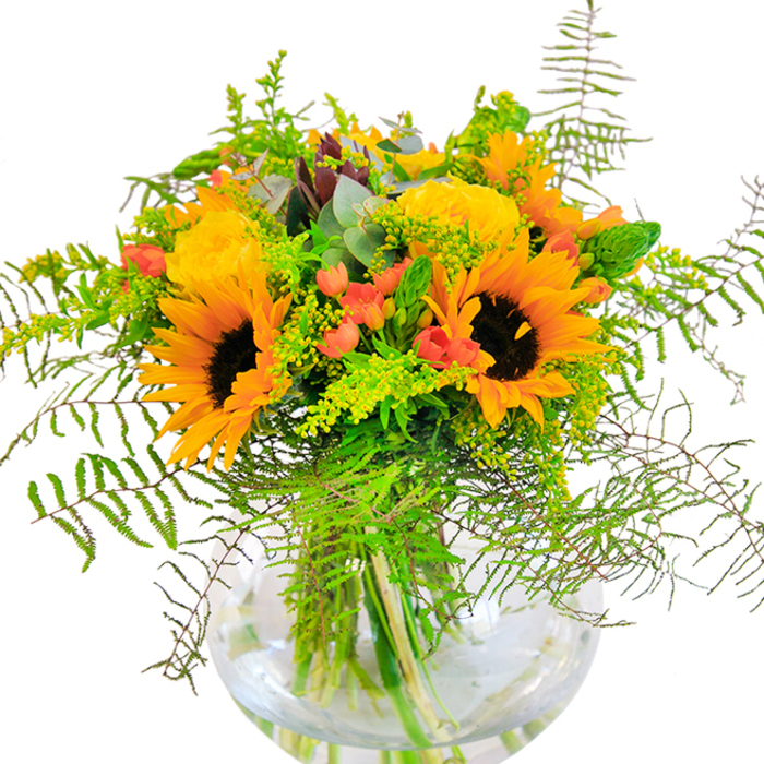 This arrangement opens with a symphony of sunlit yellow, inviting you into the golden heart of West Wickham's blooming season. Bold sunflowers and elegant yellow garden roses, their petals unfolding in luminous layers, stand side by side, radiating cheer and generosity. Stems of glossy red Hypericum berries shine through the greens, their hue a vibrant contrast to the soft blush and matte gold of the petals. Cascading outwards, airy ferns and light solidago sprigs hint at the wild beauty of local heaths and gardens, bringing a sense of movement as though the flowers themselves were caught in a gentle breeze across Bethlem Royal's fields. Slender spikes and supple eucalyptus leaves lend a fresh coolness, rounding out the texture palette. Each stem is showcased in a modern spherical glass vase-the water amplifying their color and structure. Up close, the interplay of supple blooms, crisp foliage, and smooth berries becomes even more inviting to the senses, bolstered by the subtle fragrance of open roses and freshly snipped greenery. Created for moments of joy-a birthday celebration in Langley Park, a significant anniversary, or simply to infuse brightness into a home-this bouquet exemplifies the artistry and heartfelt approach that have become synonymous with West Wickham's best floristry.